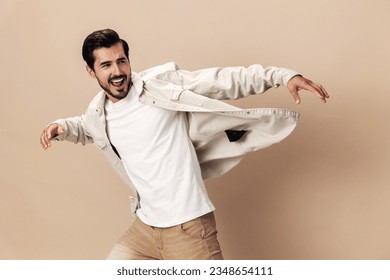 白いTシャツとビジネスジャケットにベージュの背景にスタイリッシュな男の笑顔が走り、ジャンプ、飛ぶ服のヒーロー、ファッショナブルな服のスタイル、コピー用スペース、テキスト用スペースの写真素材