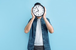 Stylish Man With A Wall Clock, Covers His Face With A Clock On A Blue Background