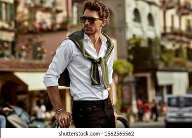 Stylish man wearing sunglasses and white shirt with tied sweater on shoulders 
