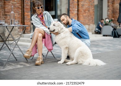 Stylish man and woman care adorable white dog while hanging out together at cafe terrace. Man flirting with woman caaring her dog - Powered by Shutterstock