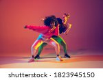 Stylish man and woman dancing hip-hop in bright clothes on green background at dance hall in neon light. Youth culture, hip-hop, movement, style and fashion, action. Fashionable portrait.