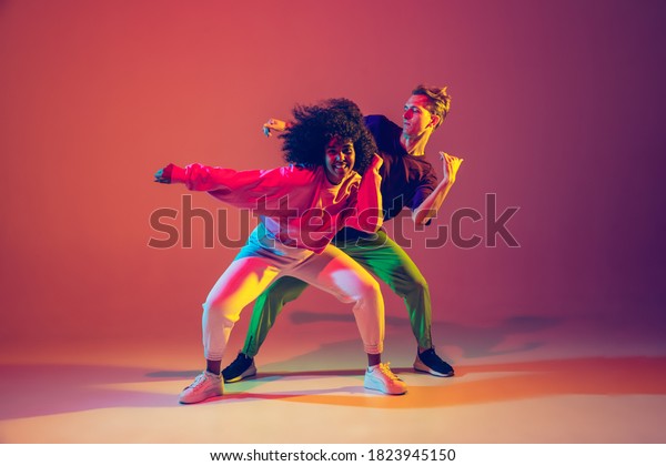 Stylish\
man and woman dancing hip-hop in bright clothes on green background\
at dance hall in neon light. Youth culture, hip-hop, movement,\
style and fashion, action. Fashionable\
portrait.