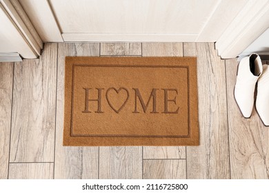 Stylish mat with word HOME near light wooden door in hallway
