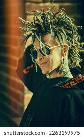 A stylish mature brutal man with ethnic tattoos and punk-style Mohawk dreadlocks wearing stylish sunglasses and ethnic black clothes. Punk and rock culture.