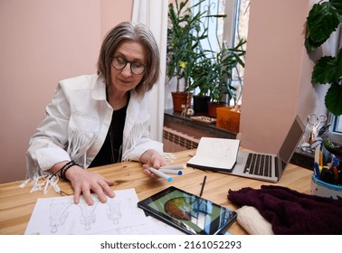 Stylish mature Caucasian woman fashion designer tailor working on color wheel on a digital tablet while sketching in tailoring atelier. Dressmaker creating garment for new collection. Business startup - Powered by Shutterstock