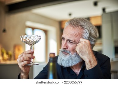 Stylish Mature Man Looking With Regret At Champagne Glass By Kitchen Table. Sober.