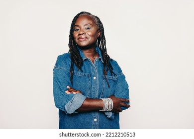 Stylish mature woman looking at the camera while standing against a grey background with her arms crossed. Fashionable woman with dreadlocks wearing a denim jacket and make-up. - Powered by Shutterstock