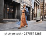 Stylish Mature Woman Walking City Street In Fashionable Clothes, Wearing Long Beige Silk Dress, Blue Cape Coat, Carrying Large Black Handbag, Sunglasses And Trendy Loafers