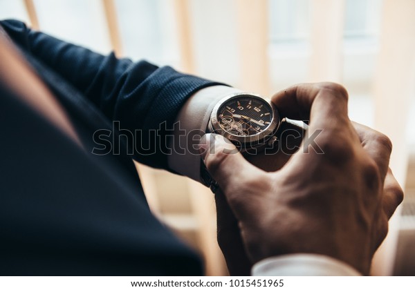 a stylish mechanical watch on\
the arm of a man dressed in a blue jacket with a white shirt that\
watches the time on the clock holding the clock by\
hand