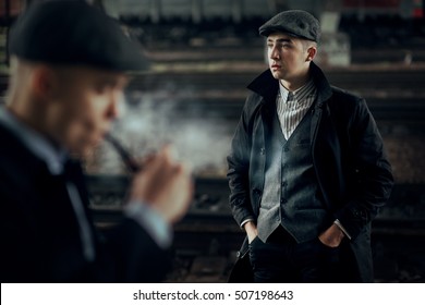 stylish men portrait in retro clothes posing on background of railway. england in 1920s theme. fashionable look of brutal confident man. atmospheric moments