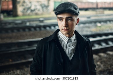 stylish men portrait in retro clothes posing on background of railway. england in 1920s theme. old fashionable look of brutal confident man. atmospheric moments