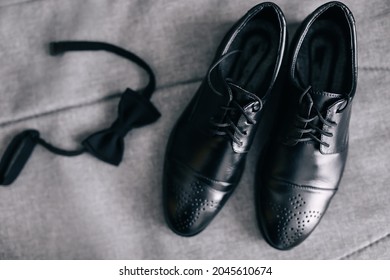 Stylish Men's Shoes On A Gray Background Next To The Shoes - A Black Bow Tie, The Groom Is Ready For The Wedding.