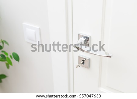 Stylish metal door handle and escutcheon for lock with key. Close-up elements of the interior. White door and white wall with switch