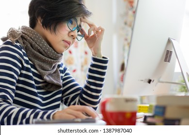 Stylish middle aged Asian woman work from home with computer through online platform during city lockdown and social distancing due to Covid-19 pandemic - look tired, stressed.