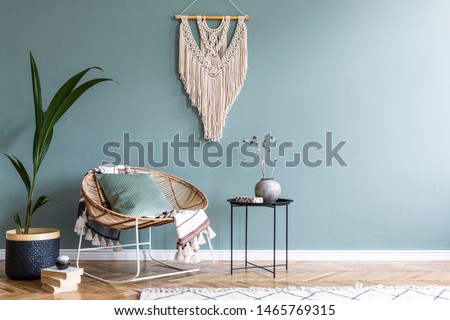 Stylish minimalistic interior of living room with design rattan armchair, black coffee table, tropical platn in basket, beige macrame on the wall and elegant accessories. Eucalyptus color of wall. 
