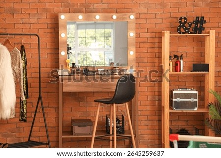 Stylish mirror, clothes rack and table with makeup cosmetics in dressing room