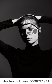Stylish model posing with fishnet headscarf, showcasing confidence and elegance against a dark monochrome background. Fashion and beauty concept.