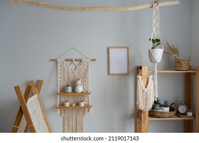 Stylish and modern boho-style nursery interior with mock-up photo frame, macrame hanging wall shelves, children's tent, wooden shelving and elegant accessories. Designer home decor. Mockup.