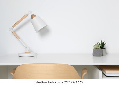 Stylish modern desk lamp and potted succulents on table near white wall indoors - Powered by Shutterstock