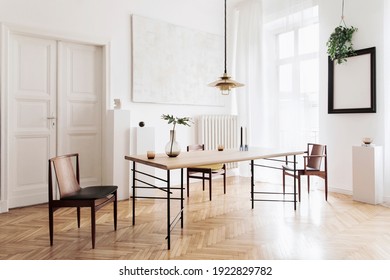 Stylish and modern dining room interior with design sharing table, chairs, gold pendant lamp, abstract paintings and elegant accessories. Tropical leafs in vase. Eclectic home decor. 