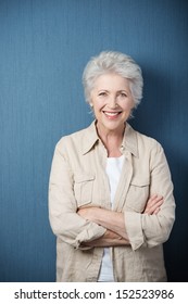 Stylish modern elderly woman standing smiling at the camera with folded arms against a green background