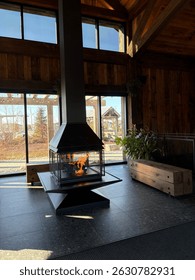 Stylish modern fireplace inside a rustic wooden lodge with sunlight streaming through large windows, creating a cozy and elegant interior design atmosphere.