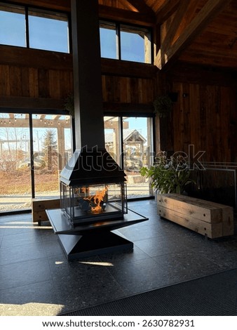 Stylish modern fireplace inside a rustic wooden lodge with sunlight streaming through large windows, creating a cozy and elegant interior design atmosphere.