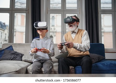 Stylish modern grandfather and grandson playing together exciting interesting video games using virtual reality headsets and gamepads at cozy home. - Powered by Shutterstock