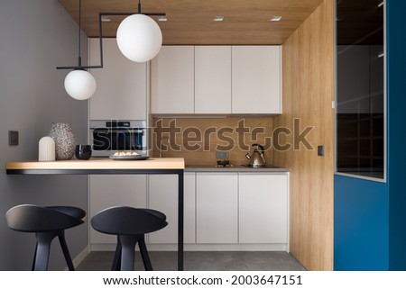 Stylish and modern kitchen with white furniture, table with two chairs and wood decor on walls, ceiling and backsplash