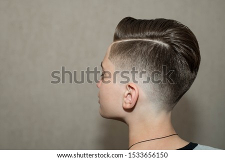 Stylish modern retro haircut side part with mid fade with parting of school boy guy in a barbershop on a brown background