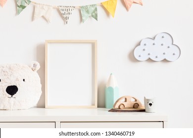 Stylish and modern scandinavian newborn baby interior with mock up photo or poster frame on the white shelf. Toys, teddy bear, wooden car and hanging cotton colorful flags and star. Template. Blank.