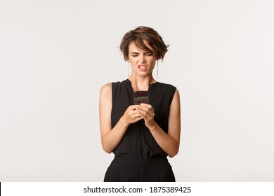 Stylish Modern Woman Looking Disgusted At Mobile Phone Screen, Cringe From Something Awful, Standing White Background