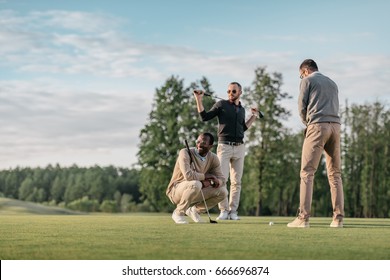 stylish multicultural friends spending time together while playing golf on golf course  - Powered by Shutterstock