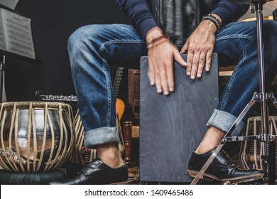 A stylish musician in denim and double monk shoes plays the Cajon, a Peruvian drum used commonly with Spain’s Flamenco dance. 
