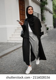 Stylish muslim woman with hijab walking and have phone conversation on the street