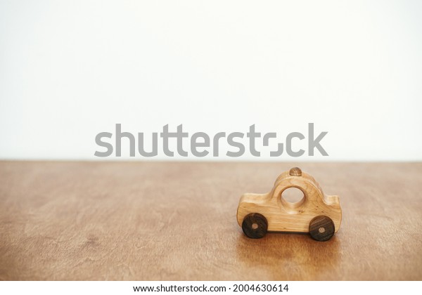 Stylish natural wooden\
car toy on table on white wall background. Space for text. Eco\
friendly plastic free toy for toddler. Stylish simple toy for\
child. Road trip and\
travel