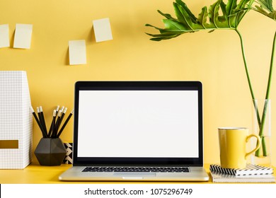 Stylish Office Workspace With Laptop Mock Up Screen, Office Accessories, Leafs On The Yellow Wall. 