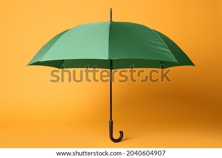 Stylish open green umbrella on yellow background