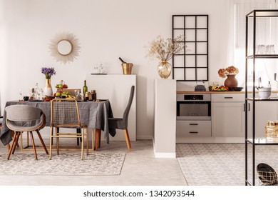 Stylish Open Plan Kitchen And Dining Room Interior With White Cupboard And Long Table With Grey Tablecloth And Food