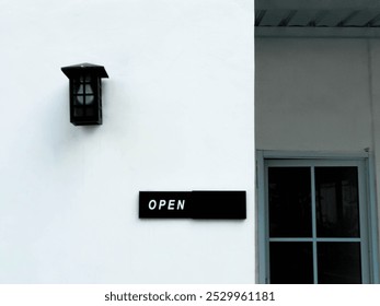 A stylish "OPEN" sign accompanied by a vintage lantern, set against a clean white wall, inviting visitors. - Powered by Shutterstock