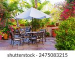 Stylish patio dining set with a white umbrella, nestled in a lush garden with vibrant flowers.