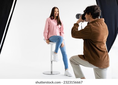 Stylish photoshoot. Male fashion photographer taking picture of young european woman in casual wear, having photosession in modern studio on white background - Powered by Shutterstock