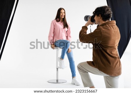 Stylish photoshoot. Male fashion photographer taking picture of young european woman in casual wear, having photosession in modern studio on white background