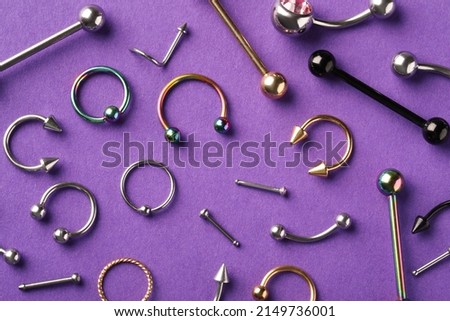 Stylish piercing jewelry on violet background, flat lay