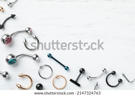 Stylish piercing jewelry on white wooden table, flat lay. Space for text