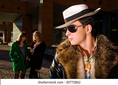 Stylish pimp in a hat and two young women on background outdoors