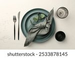 Stylish plates, cutlery, napkin, sauce bowl, glass and eucalyptus branch on beige textured table, top view