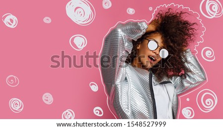 Stylish playful girl  dancing and playing with curly hairs on pink background. Party mood. 