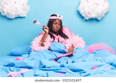 Stylish Plump Adult African American Woman Keeps Lips Folded Makes List To Do Writes Down Something Holds Pen In Hand Wears Dressing Gown Wears Comforrtable Dressing Gown Poses At Bedroom Alone