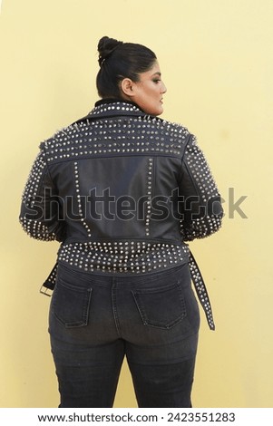 stylish plus sized female model posing in beautiful black leather jacket and jeans with high heels and bun